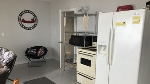 Een kleine keuken met een koelkast, magnetron, oven en een hangrek.