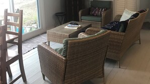 Een woonkamer met rieten meubilair, een flatscreen televisie en een schuifdeur met glas.