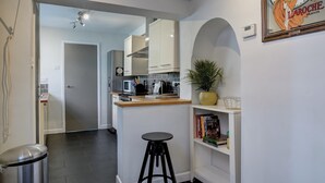 Eine moderne Küche mit weißen Schränken, einem schwarzen Hocker, einer Mikrowelle und einem Blumentopf.