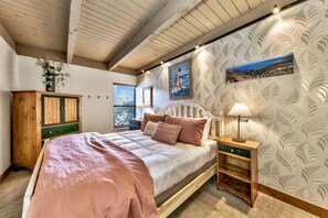Um quarto com cama, mesa de cabeceira, armário de madeira e janela com persianas.