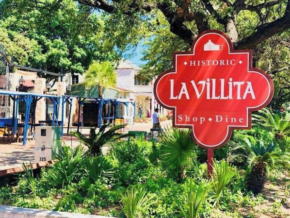 A red sign with 'LAVILLITA Shop · Dine' and 'HISTORIC' written on it, surrounded by greenery and a building in the background. - Beautiful Fenced 3BR 2BA Near Exciting Downtown (San Antonio)