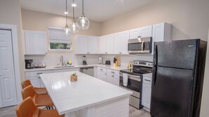 A modern kitchen with white cabinets, a black refrigerator, and a central island with chairs.