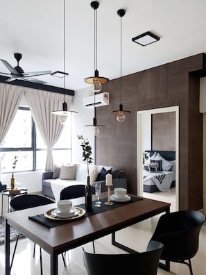 A modern dining area with a wooden table, black chairs, pendant lights, and a view of a living room with a sofa and a bed.