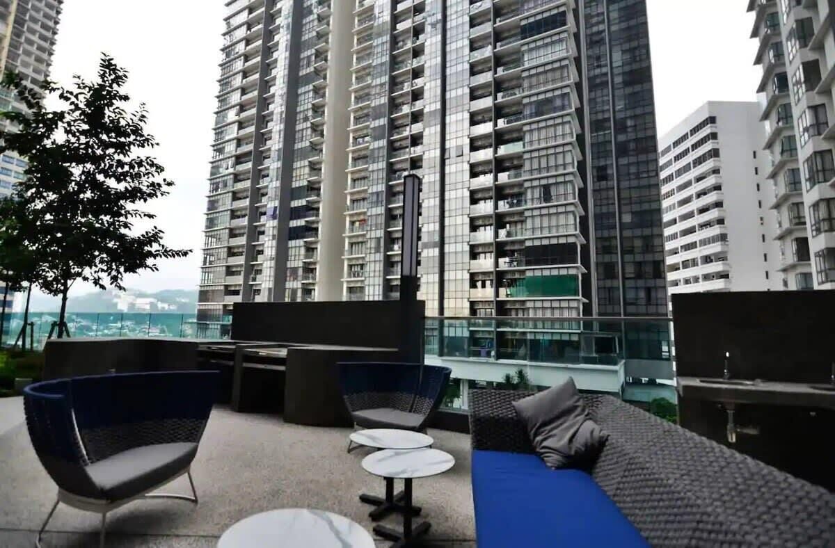 Um lounge no terraço com móveis modernos, vista para edifícios altos e guarda-corpo de vidro.