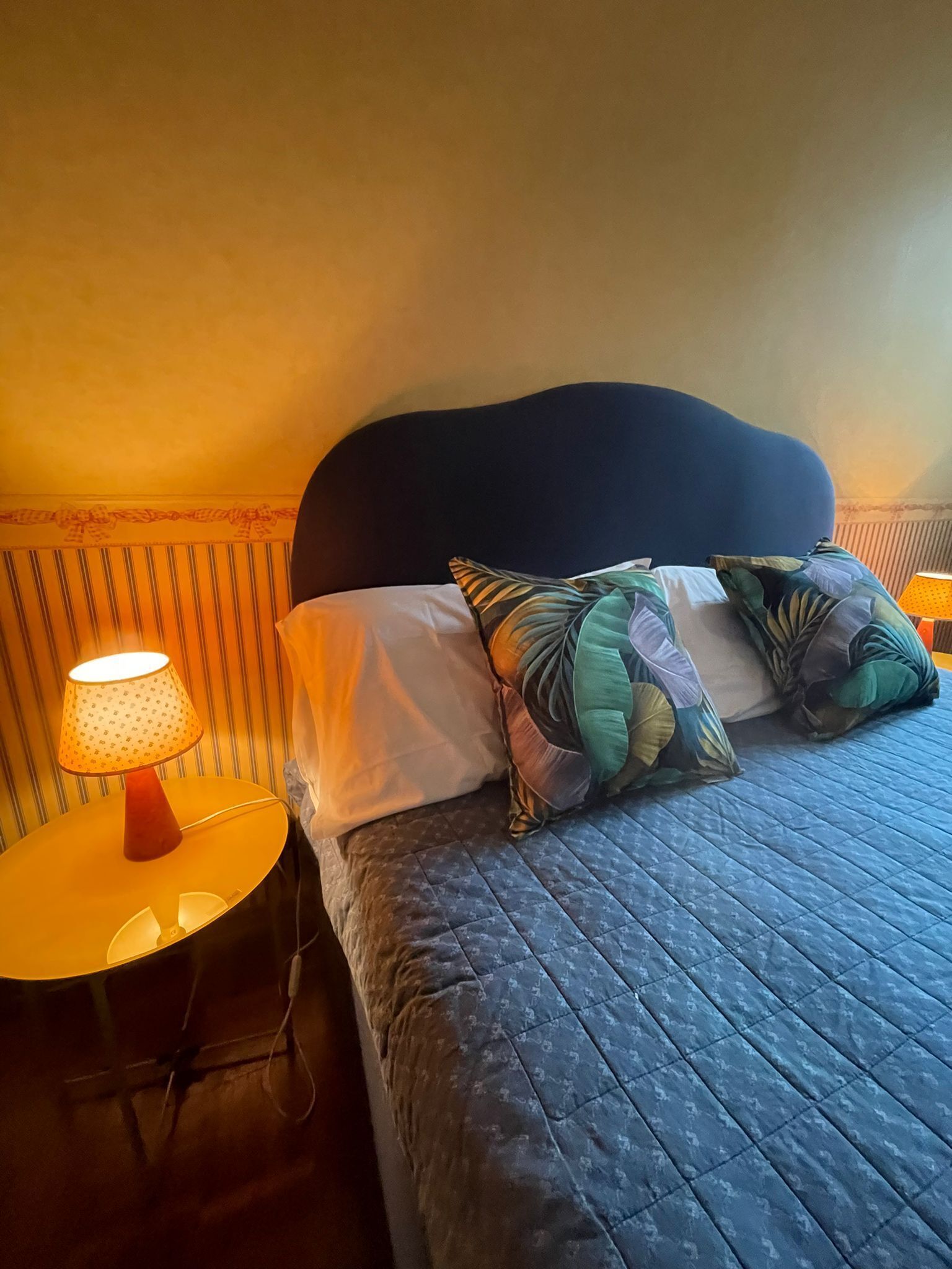 A bedroom with a bed, a bedside table with a lamp, and a striped wall.