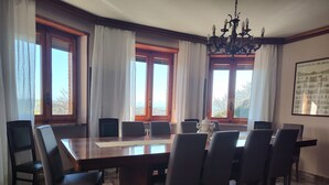 A conference room with a large wooden table, six chairs, a chandelier, and large windows with curtains.
