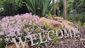 A garden with a 'WELCOME' sign, various plants, and a building in the background.