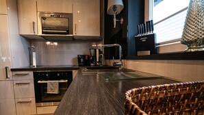 A modern kitchen with a dark wood countertop, stainless steel appliances, and a wicker chair. - country-apartment XL for 2-4 persons (Braunlage)