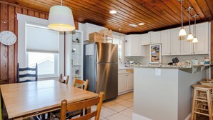 A kitchen with wooden ceiling, white cabinets, stainless steel appliances, and a dining area with wooden chairs and a table. - Pet friendly home w yard across from beach (Kure Beach)