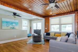 Relax in this stylish living room with a high ceiling, featuring a grey sofa, armchair, and a beautiful beach scene painting.