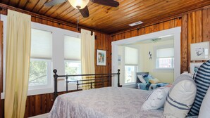 A bedroom with a wooden ceiling, a bed with patterned bedding, and a view of another room through an open door. - Pet friendly home w yard across from beach (Kure Beach)