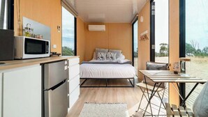 Un dormitorio compacto con cama, una kitchenette pequeña y vistas a través de amplios ventanales.