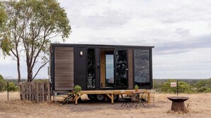 Una casa móvil moderna y compacta con un amplio ventanal corredero, una pequeña terraza y una mesa de picnic.