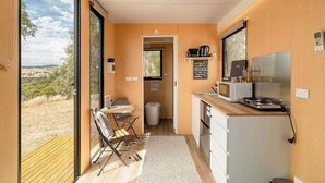 Cocina compacta con comedor, vista a través de un ventanal y un pequeño cubo de basura.