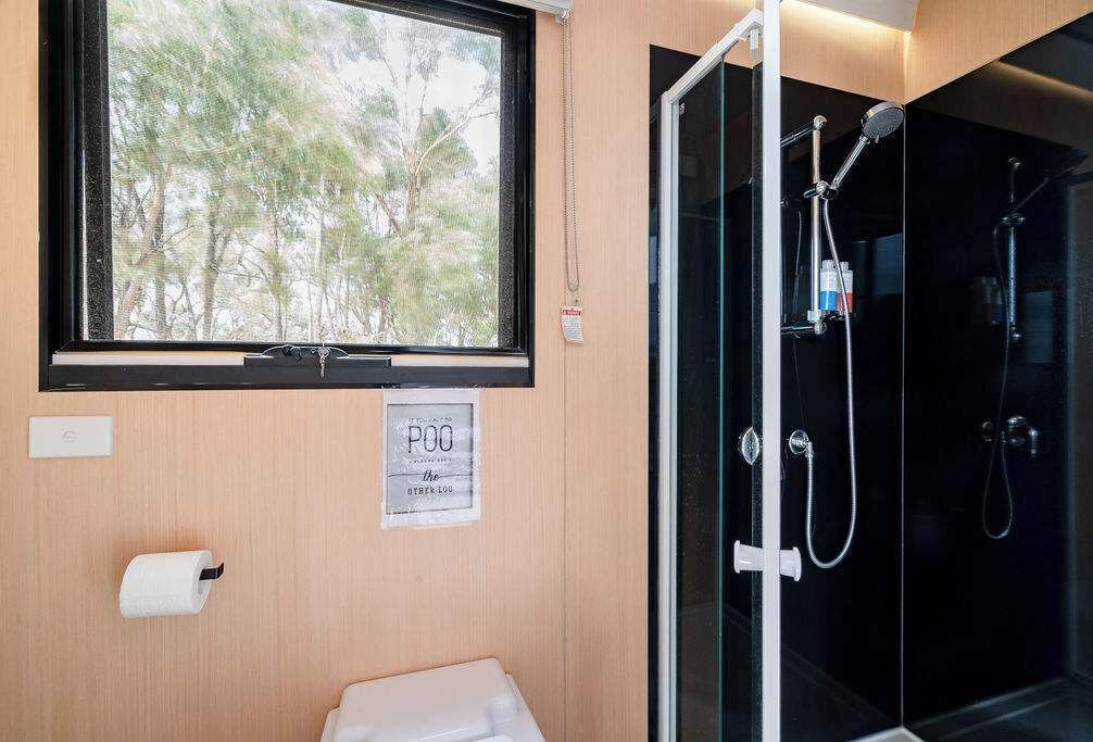A bathroom with a toilet, a window with a view of trees, and a glass-enclosed shower area.