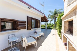 A patio area with a white wall, wooden shutters, a small table with a potted plant, and two white lounge chairs. - Villetta Casetta Li Foggi (Gallipoli)