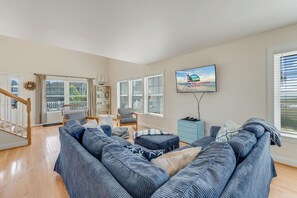 A living room with a large sectional sofa, a television mounted on the wall, and a staircase leading to another level.