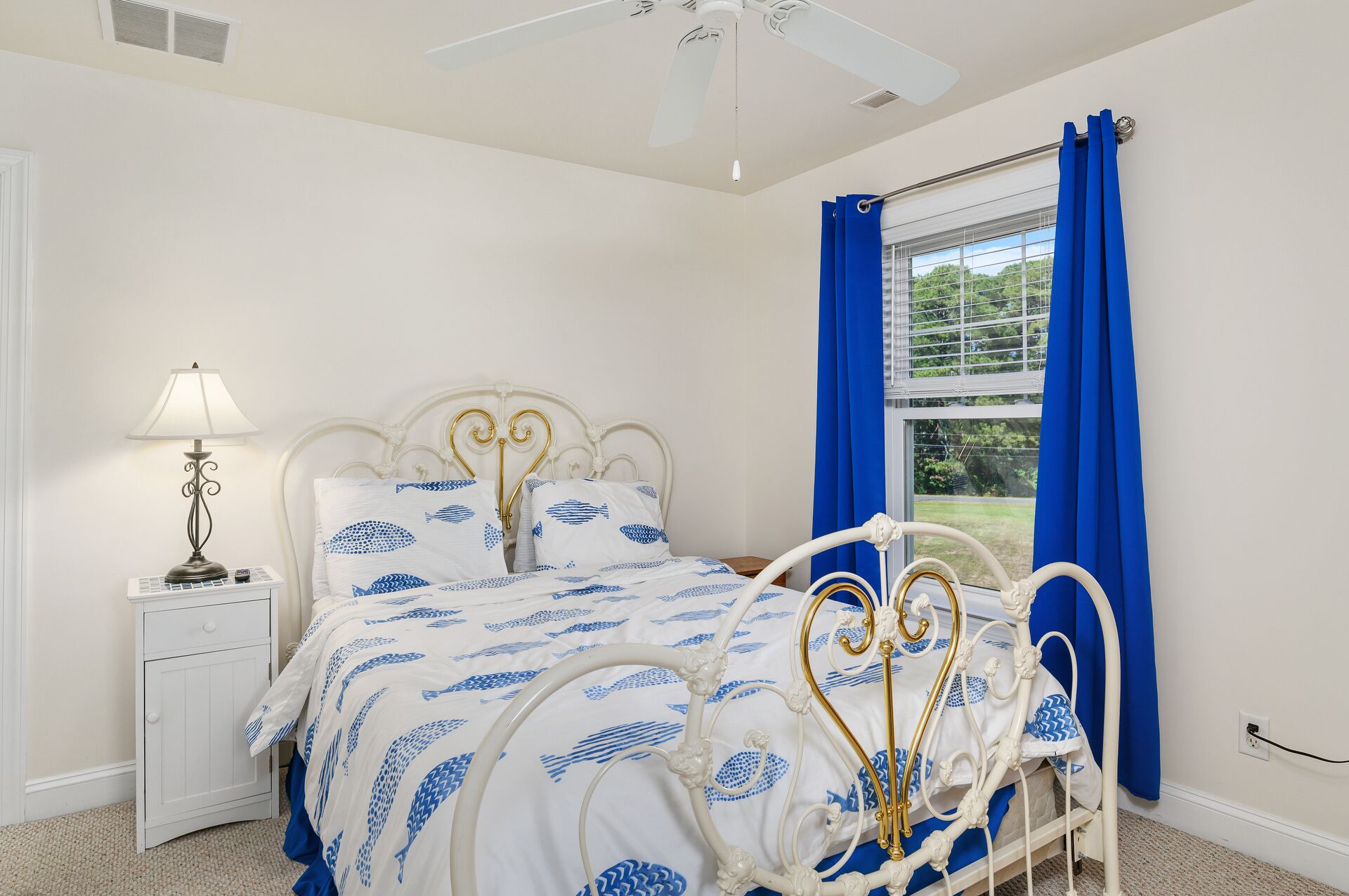 A bedroom with a white bed, blue curtains, and a ceiling fan.