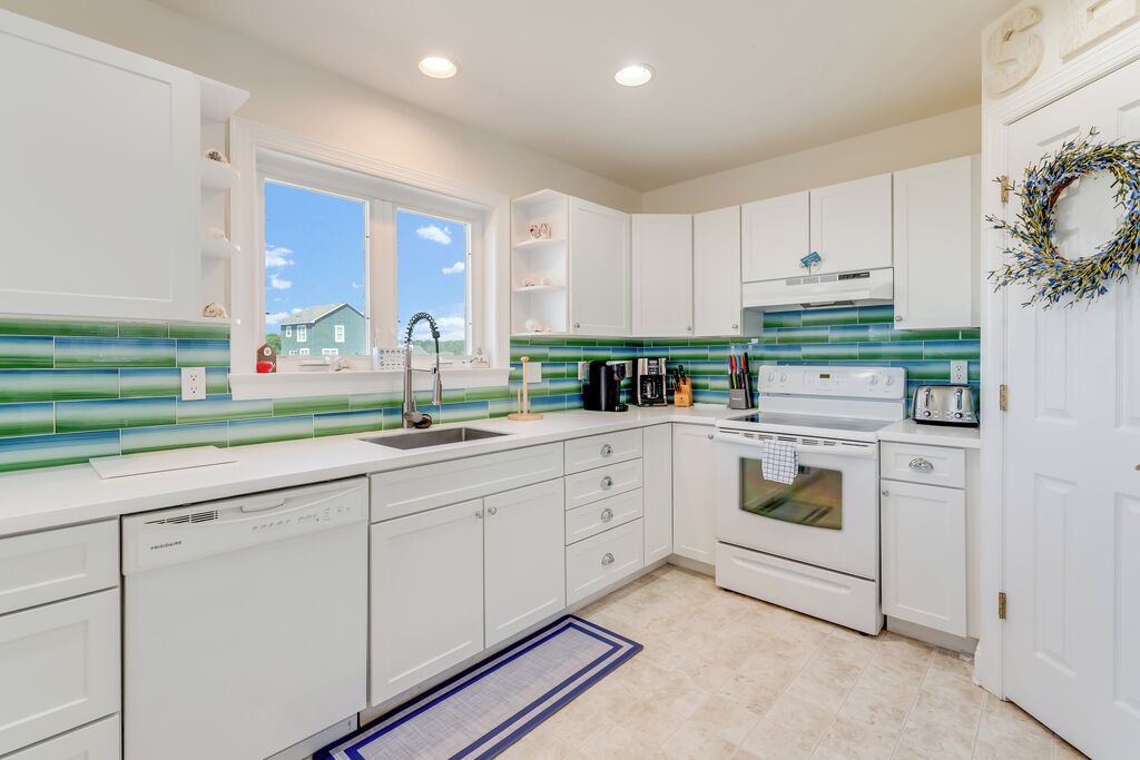 A modern kitchen with white cabinets, a dishwasher, a stove, and a window.