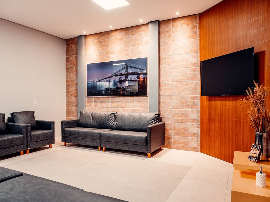 Un salon moderne avec un canapé gris, deux fauteuils, un téléviseur à écran plat et un tableau représentant un paysage urbain, encadré et accroché au mur.