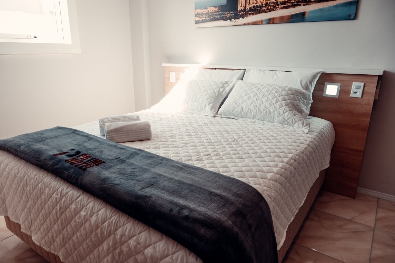 A neatly made bed with a quilted cover and a dark blanket, a wooden headboard, and a wall-mounted light fixture.