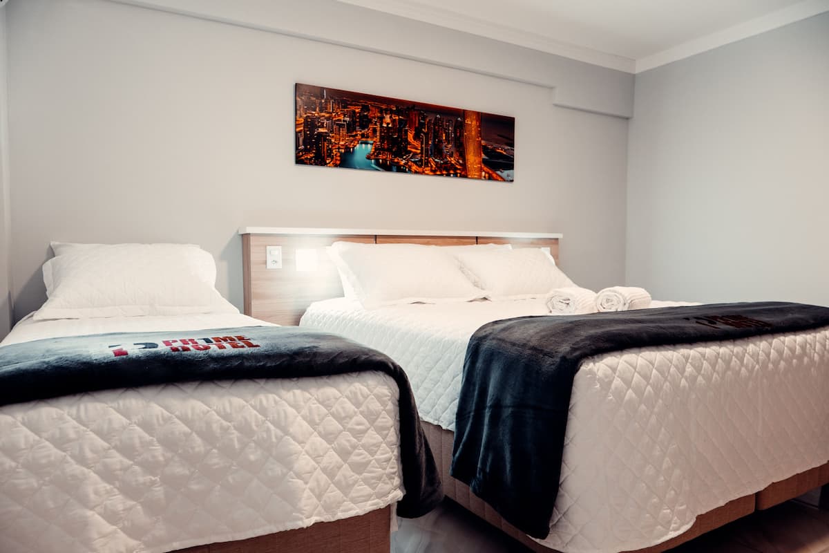 Une chambre d’hôtel avec deux lits, un tableau représentant un paysage urbain accroché au mur et une vue sur la ville de nuit.