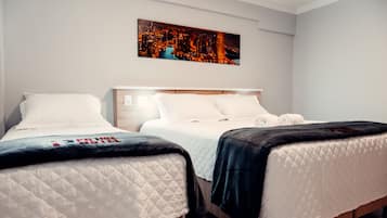 A hotel room with two beds, a cityscape painting on the wall, and a view of the city at night.