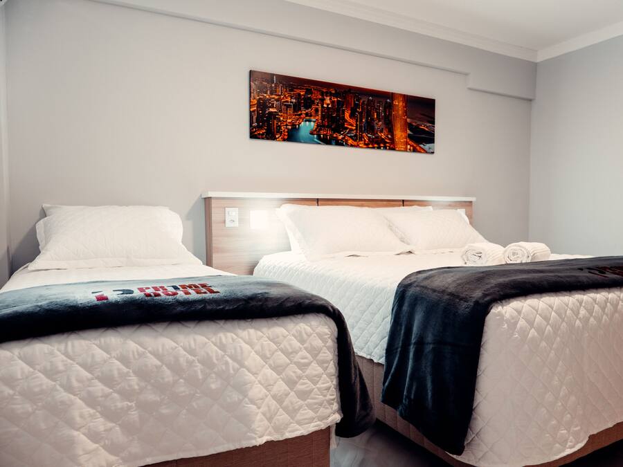 A hotel room with two beds, a cityscape painting on the wall, and a view of the city at night.