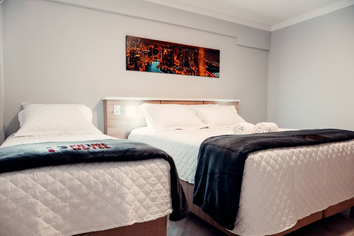Une chambre d’hôtel avec deux lits, une œuvre d’art représentant un paysage urbain accrochée au mur et une vue sur la ville.