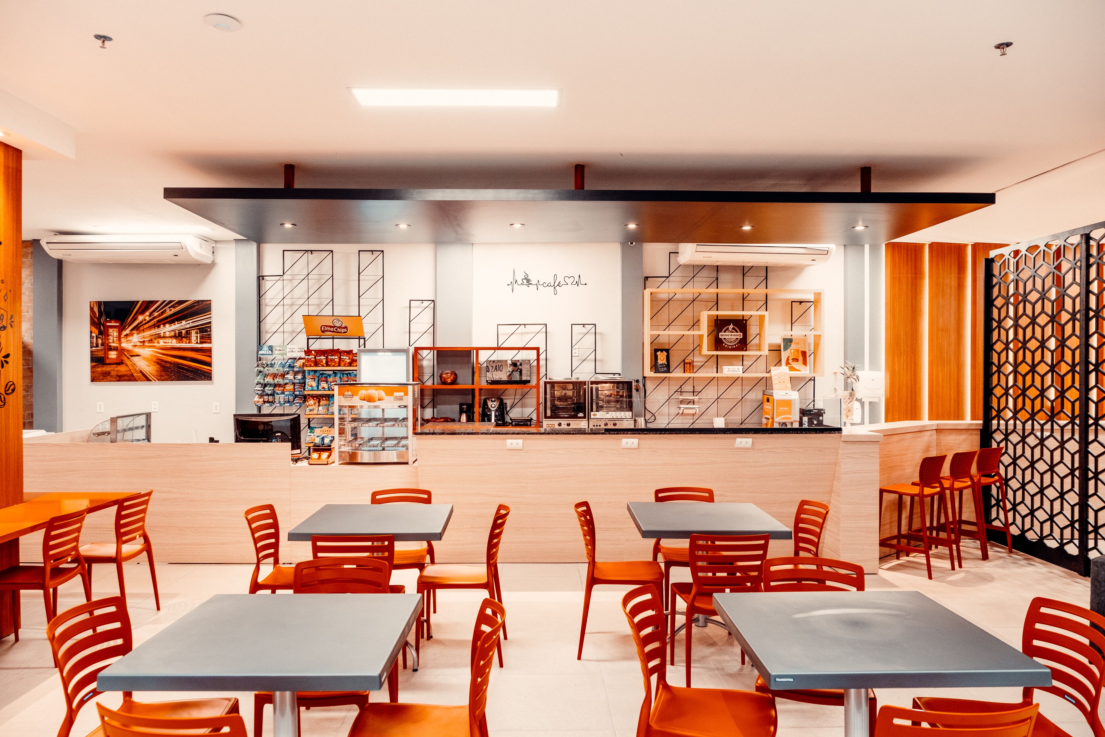 A modern cafe with tables and chairs, a counter with a menu, and a wall with a geometric pattern.