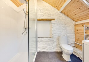 Compact bathroom with a glass shower enclosure, handheld showerhead, and a white toilet.