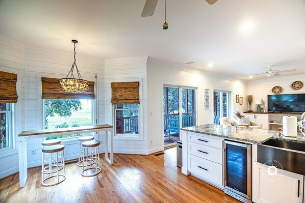 A modern kitchen with a bar area, wooden flooring, and large windows offering a view of the outdoors.