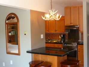 A kitchen with wooden cabinets, a black countertop, a chandelier, and a built-in oven. - Mountain views, walk to downtown Estes, The Bunkhouse @ Old Man Mountain Studios (Estes Park)