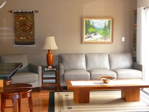 A living room with a sofa, coffee table, and a lamp. There is a painting on the wall and a rug on the floor. - Mountain views, walk to downtown Estes, The Bunkhouse @ Old Man Mountain Studios (Estes Park)
