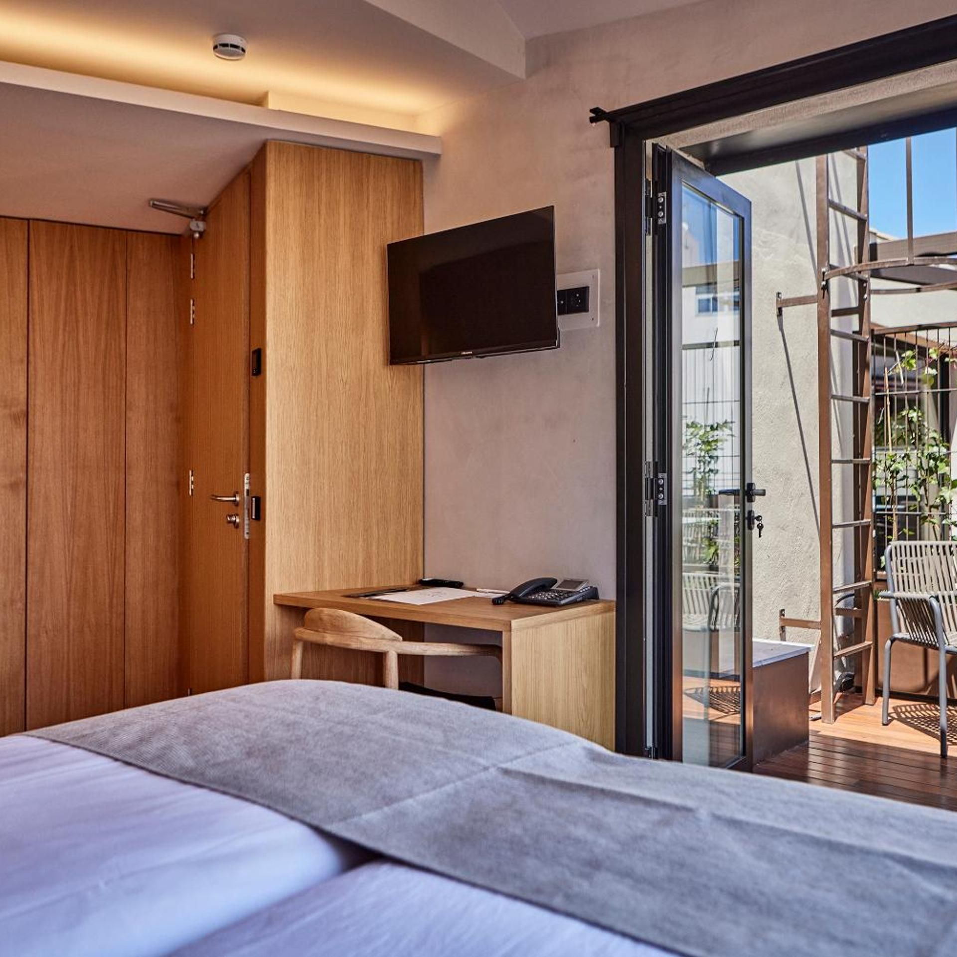Una moderna camera d'albergo con un letto, una scrivania, una sedia, una televisione e una porta scorrevole in vetro che dà su una zona esterna.