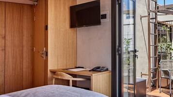 Una moderna camera d'albergo con un letto, una scrivania, una sedia, una televisione e una porta scorrevole in vetro che dà su una zona esterna.
