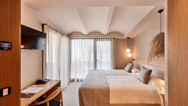 A hotel room with a bed, a desk, a TV, and a large window with curtains. - Joe´s Gomila Boutique Hotel (Palma)