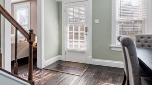 Una habitación con escalera de madera, una puerta blanca con ventanal y una zona de comedor con mesa y sillas.