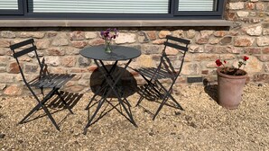A patio with a round table and two chairs, a vase with flowers, and a potted plant. - Cosy countryside retreat, edge of Frome near Bath. Pets welcome. (Mells, Frome)