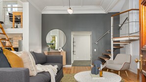 Ein modernes Wohnzimmer mit einem grauen Sofa, einem runden Couchtisch und einer Treppe mit Holzwandung.