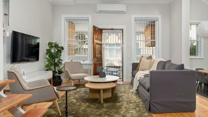 Ein modernes Wohnzimmer mit rundem Couchtisch, einem grauen Sofa, einem beige farbenen Sessel und einem Fernseher an der Wand.