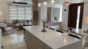 Una cocina moderna con una isla central, un comedor con una mesa redonda y una sala de estar con un sofá y una mesa de centro.