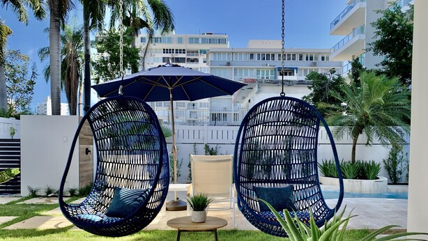 Un área de estar moderna al aire libre con dos sillas de mimbre azules, una mesita redonda y una planta en maceta.