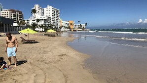 Una playa con arena, sombrillas y un edificio al fondo.
