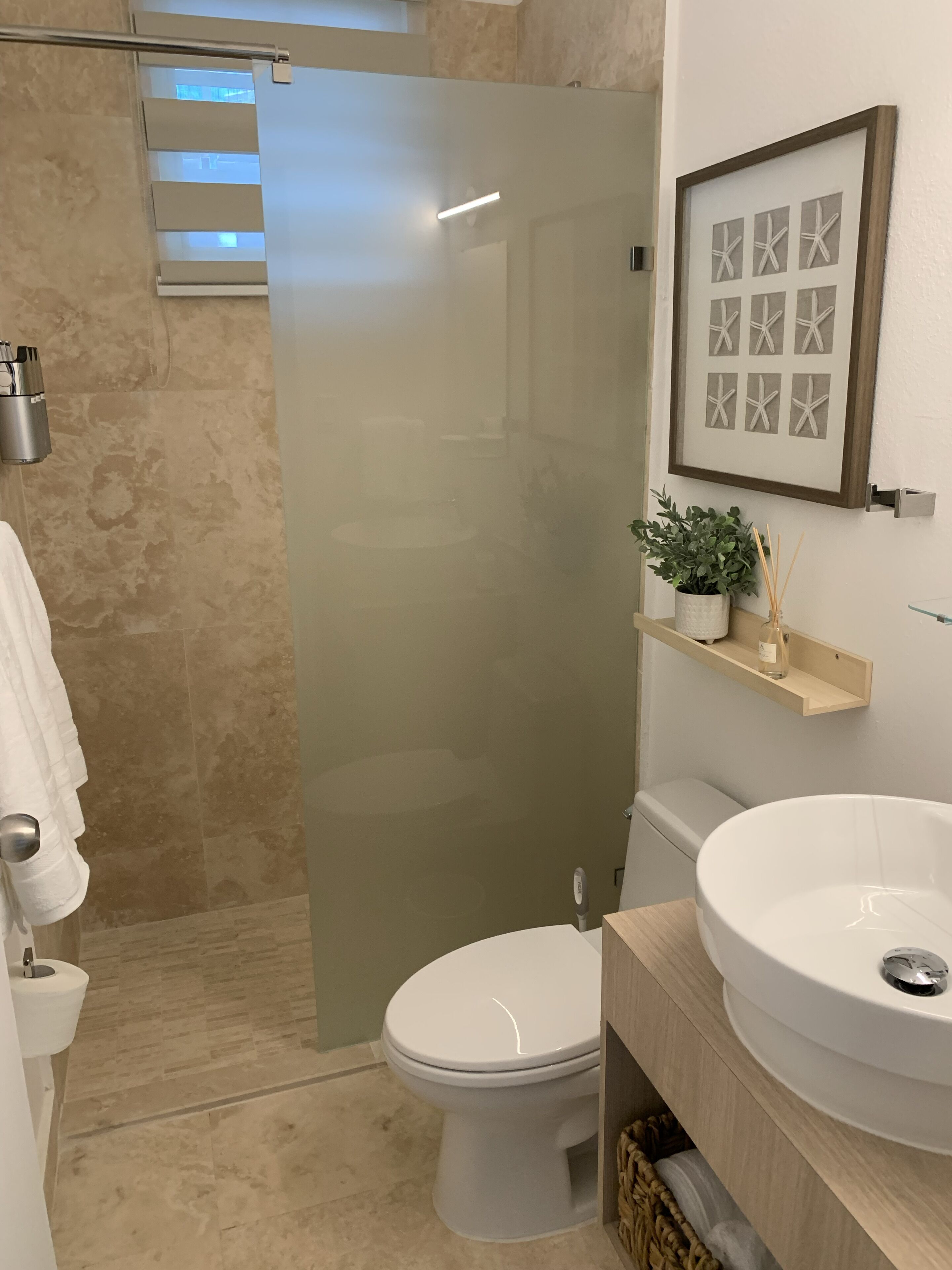 Une salle de bain moderne avec une porte de douche en verre, des toilettes, un lavabo et un tableau encadré représentant des étoiles de mer accroché au mur.