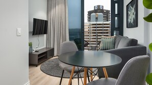 Un salon moderne avec une table ronde, un canapé gris et un téléviseur fixé au mur.