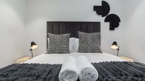Une chambre à coucher moderne avec un grand lit, deux coussins aux motifs noir et blanc, une tête de lit sombre et deux lampes de chevet.
