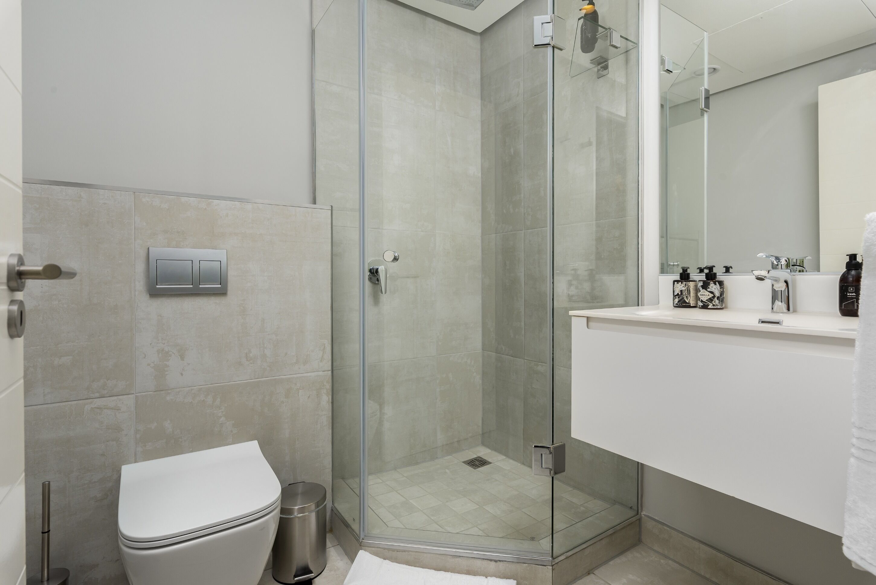 Une salle de bain moderne avec une douche à parois de verre, des toilettes blanches et un meuble-lavabo doté d’un miroir et d’articles de toilette.