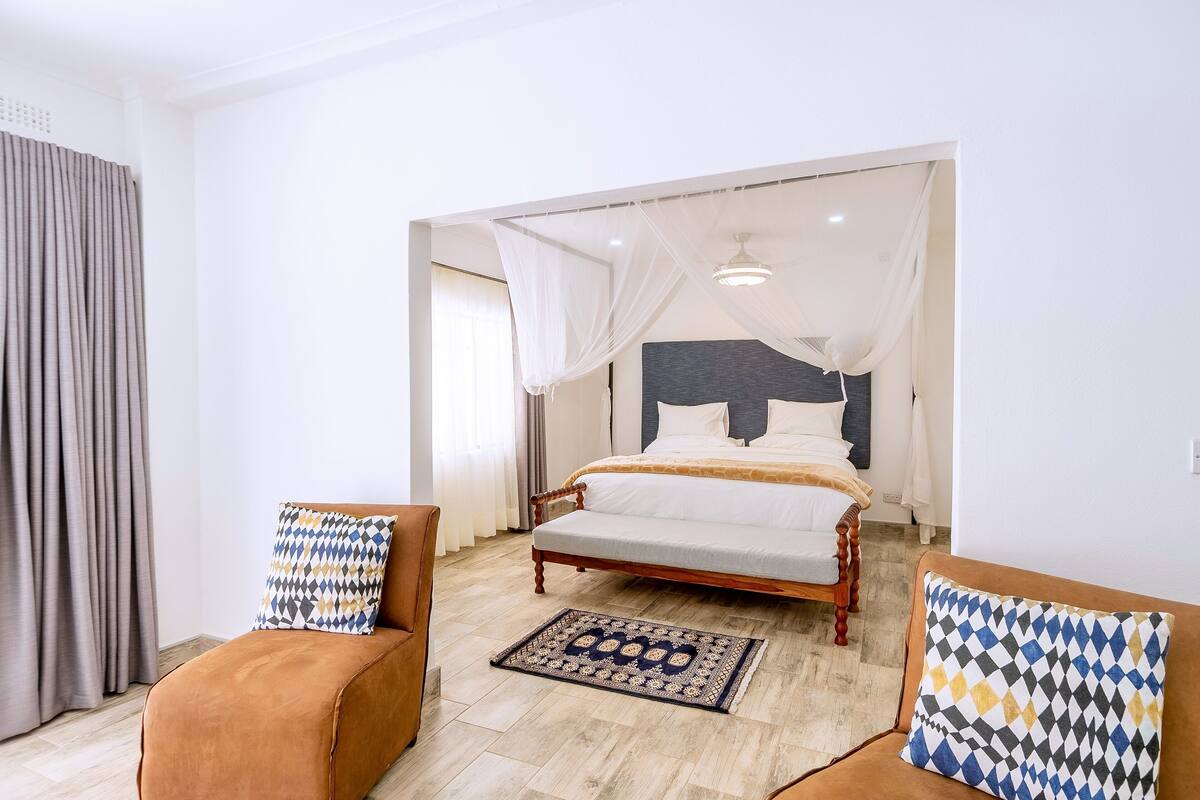 Une chambre à coucher comprenant un lit, deux fauteuils, une table de chevet et une commode.