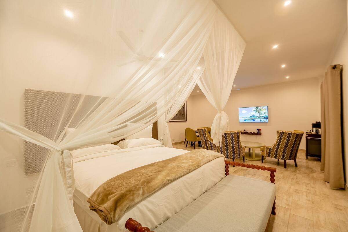 Une chambre à coucher avec un lit à baldaquin, une télévision et un bureau avec des chaises.